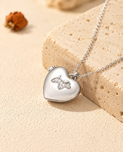 Personlig hjärtmedaljong i silverfärgat utförande med en valp i zirkonia på locket, lutad mot ett travertinblock