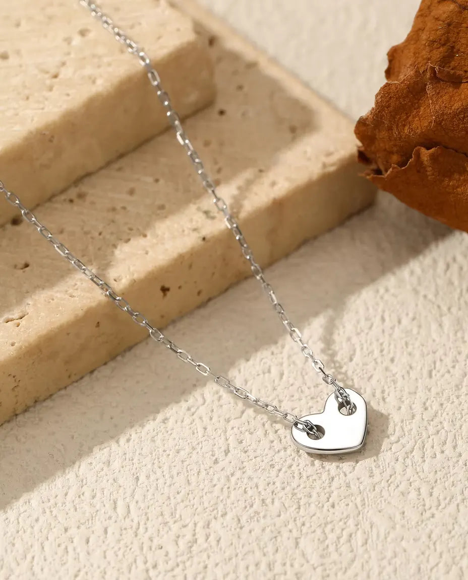 Halsband med Hjärta i 925 Sterlingsilver - hänget på en ljus yta bredvid en travertinplatta