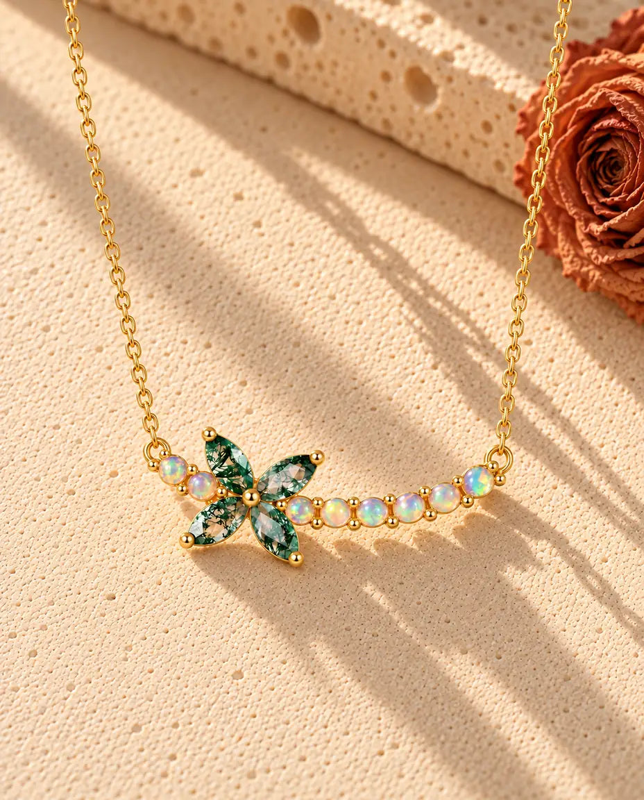 Moss Agate Halsband med Blomma i Guldpläterat 925 Sterlingsilver - liggande på en ljus strukturerad yta bredvid ett travertinblock