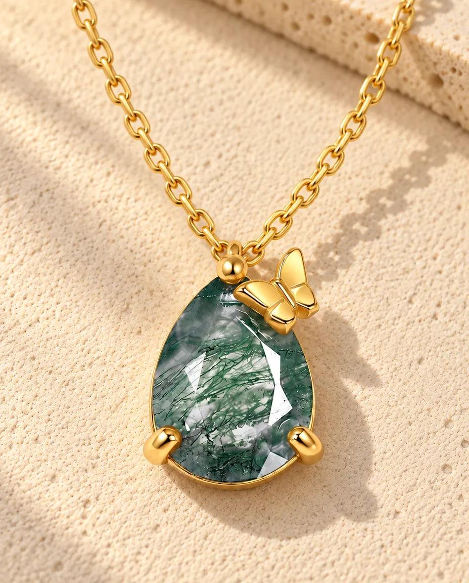 Moss Agate Halsband i Guldpläterat 925 Sterlingsilver - liggande på en ljus strukturerad yta bredvid ett travertinblock