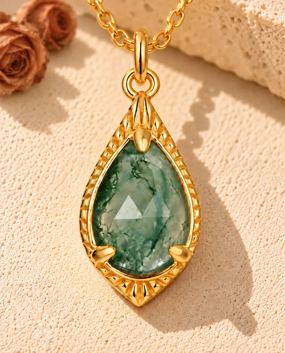 Moss Agate Halsband i Guldpläterat 925 Sterlingsilver - liggande på en ljus strukturerad yta bredvid ett travertinblock