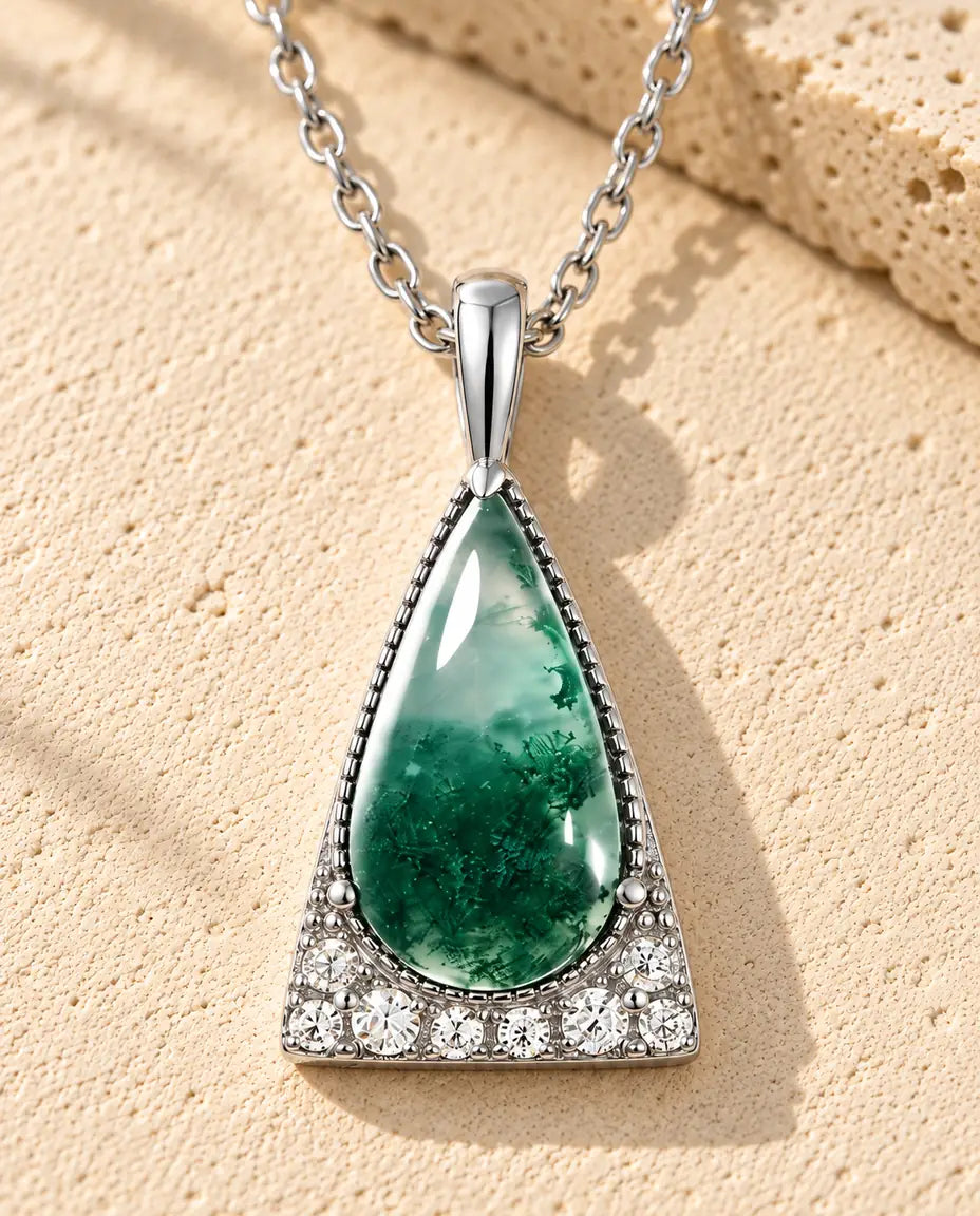 Moss Agate Halsband med Triangel i 925 Sterlingsilver - liggande på en ljus strukturerad yta bredvid ett travertinblock