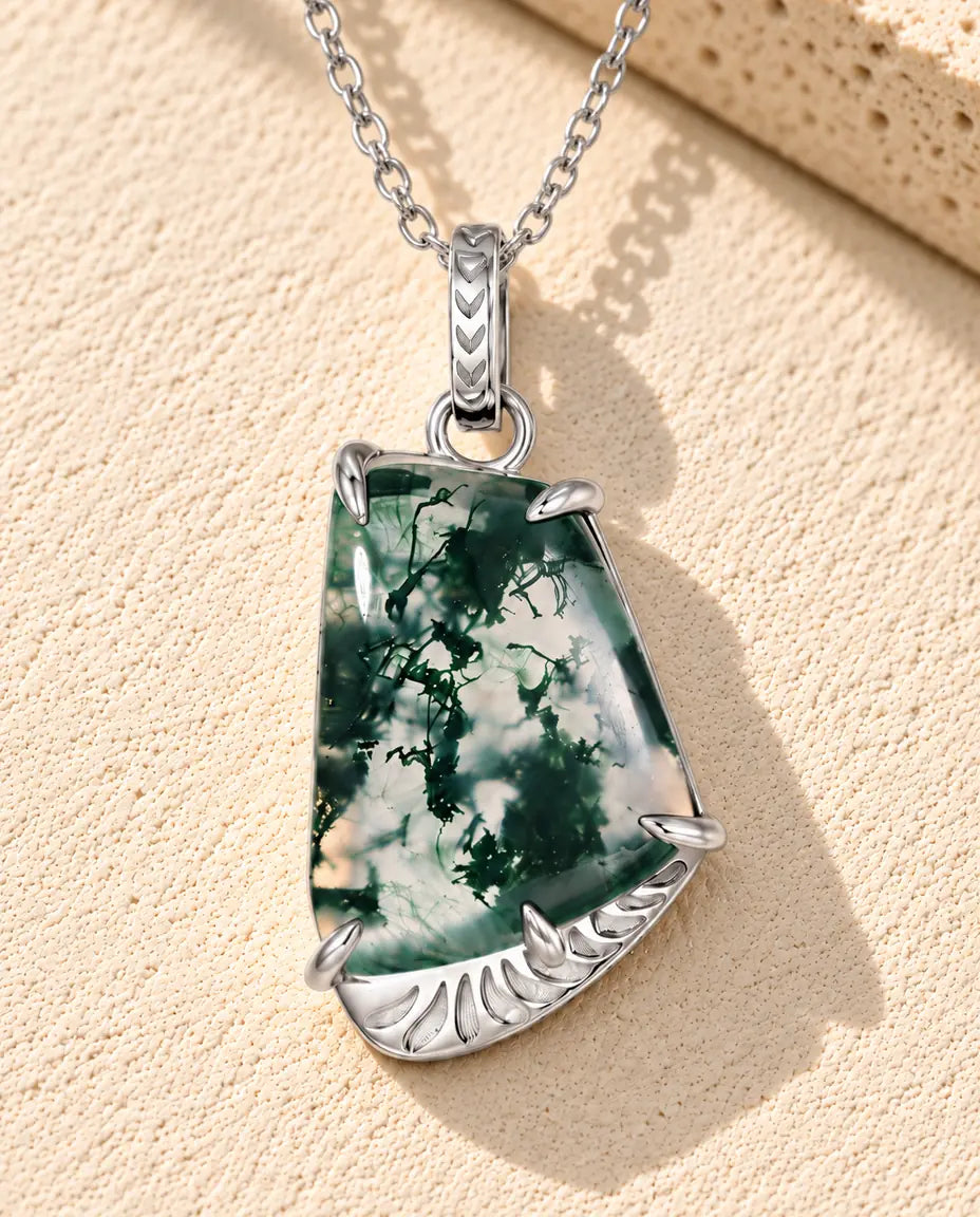 Moss Agate Halsband i Fri Form i 925 Sterlingsilver - liggande på en ljus strukturerad yta bredvid ett travertinblock