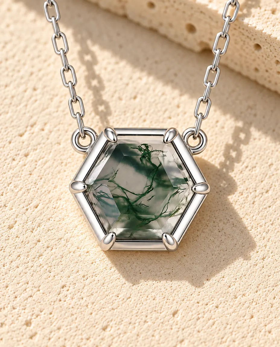 Hexagonal Moss Agate Halsband i 925 Sterlingsilver - liggande på en ljus strukturerad yta bredvid ett travertinblock