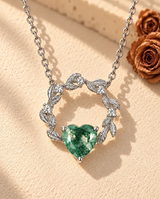 Moss Agate Halsband med Hjärta i 925 Sterlingsilver - liggande på en ljus strukturerad yta bredvid ett travertinblock