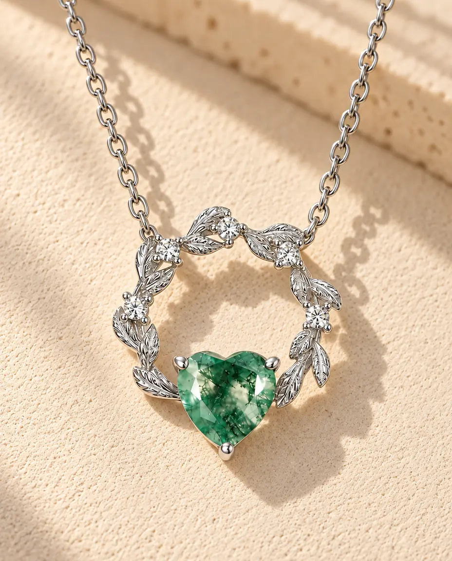 Moss Agate Halsband med Hjärta i 925 Sterlingsilver - liggande på en ljus strukturerad yta bredvid ett travertinblock