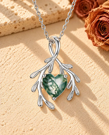 Moss Agate Halsband med Hjärta och Grenar i 925 Sterlingsilver - liggande på en ljus strukturerad yta bredvid ett travertinblock