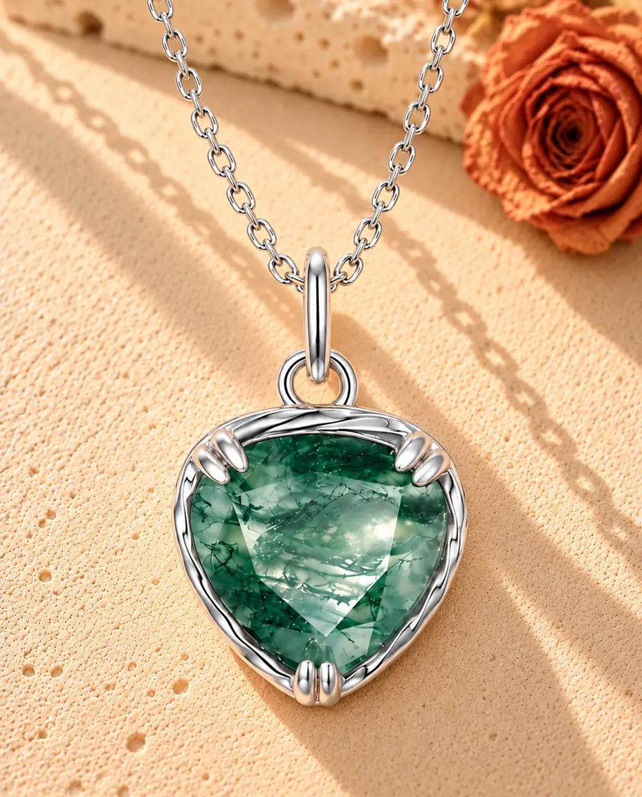 Moss Agate Halsband med Hjärta i 925 Sterlingsilver - liggande på en ljus strukturerad yta bredvid ett travertinblock