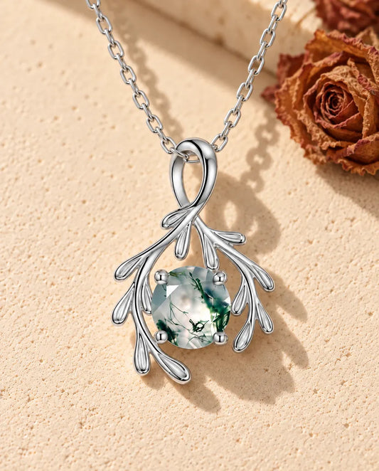 Moss Agate Halsband med Silvergrenar i 925 Sterlingsilver - liggande på en ljus strukturerad yta bredvid ett travertinblock