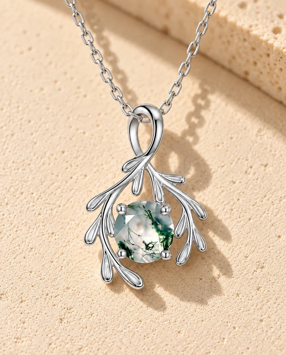 Moss Agate Halsband med Silvergrenar i 925 Sterlingsilver - liggande på en ljus strukturerad yta bredvid ett travertinblock