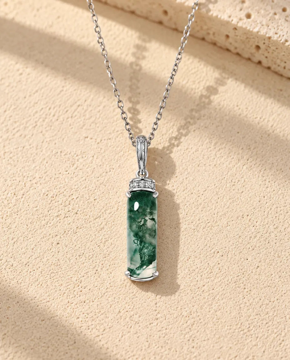 Moss Agate Halsband med Lång Stav i 925 Sterlingsilver - liggande på en ljus strukturerad yta bredvid ett travertinblock