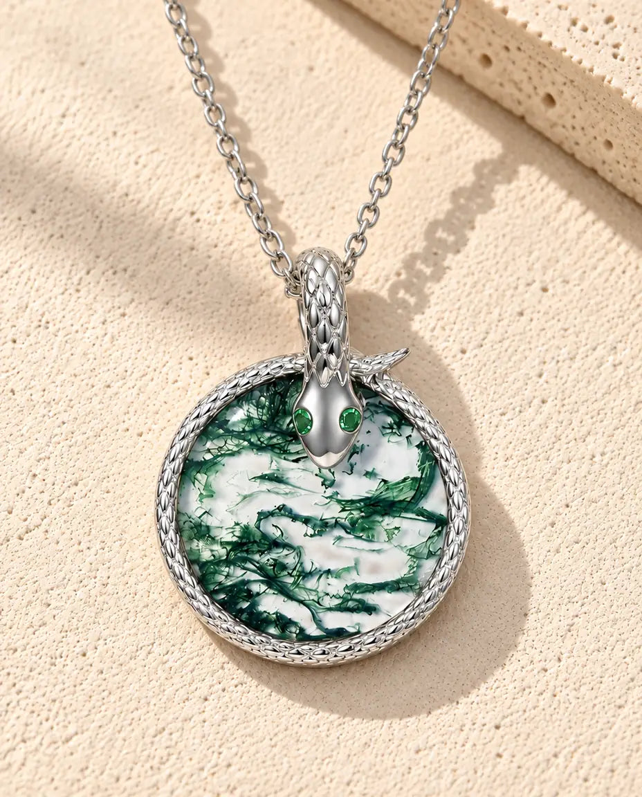 Moss Agate Halsband med Orm i 925 Sterlingsilver - liggande på en ljus strukturerad yta bredvid ett travertinblock
