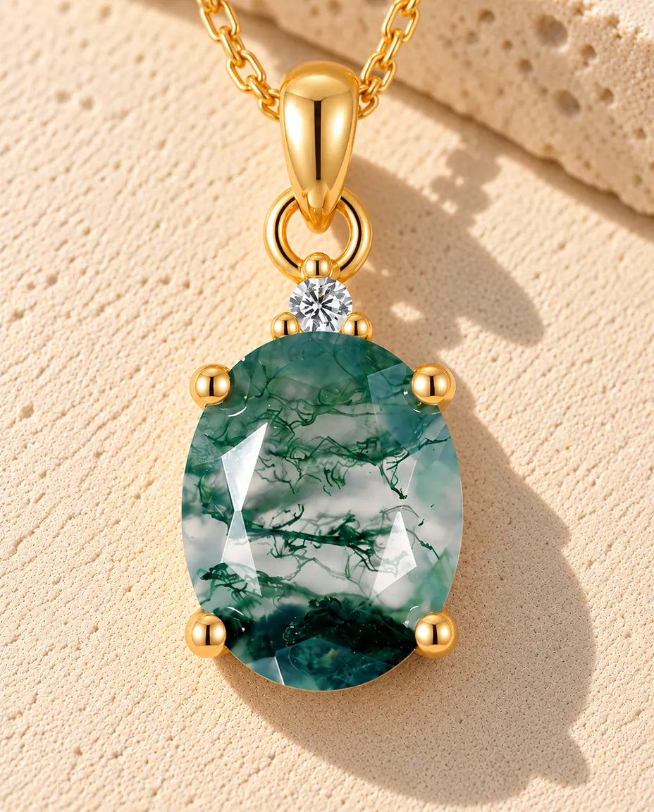 Moss Agate Halsband i Guldpläterat 925 Sterlingsilver - liggande på en ljus strukturerad yta bredvid ett travertinblock
