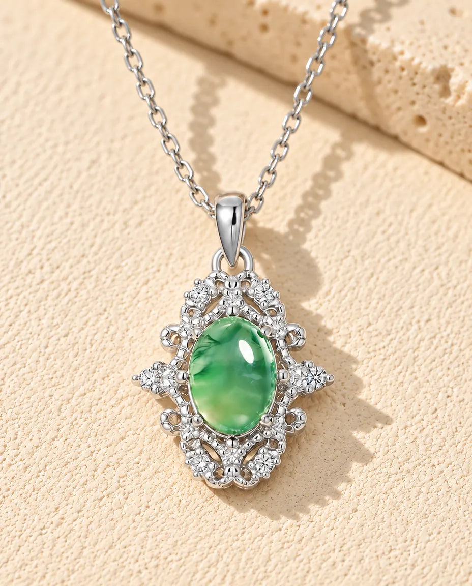 Moss Agate Halsband med Oval Cabochon i 925 Sterlingsilver - liggande på en ljus strukturerad yta bredvid ett travertinblock