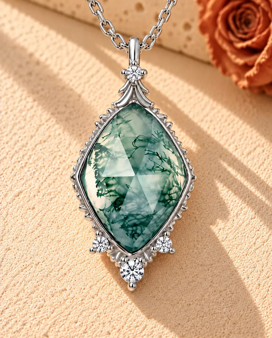 Moss Agate Halsband med Romb i 925 Sterlingsilver - liggande på en ljus strukturerad yta bredvid ett travertinblock