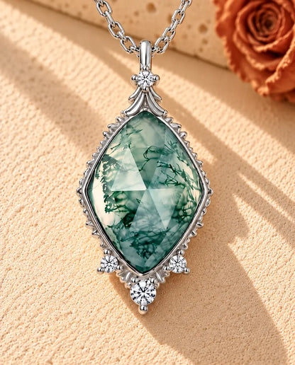 Moss Agate Halsband med Romb i 925 Sterlingsilver - liggande på en ljus strukturerad yta bredvid ett travertinblock