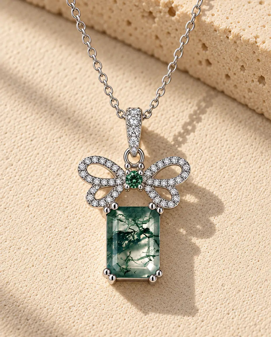Moss Agate Halsband med Rosett i 925 Sterlingsilver - liggande på en ljus strukturerad yta bredvid ett travertinblock