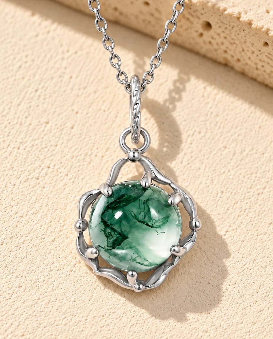 Moss Agate Halsband Rund i 925 Sterlingsilver - liggande på en ljus strukturerad yta bredvid ett travertinblock