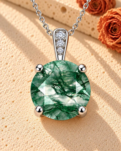 Moss Agate Halsband med Rund Solitär i 925 Sterlingsilver - liggande på en ljus strukturerad yta bredvid ett travertinblock