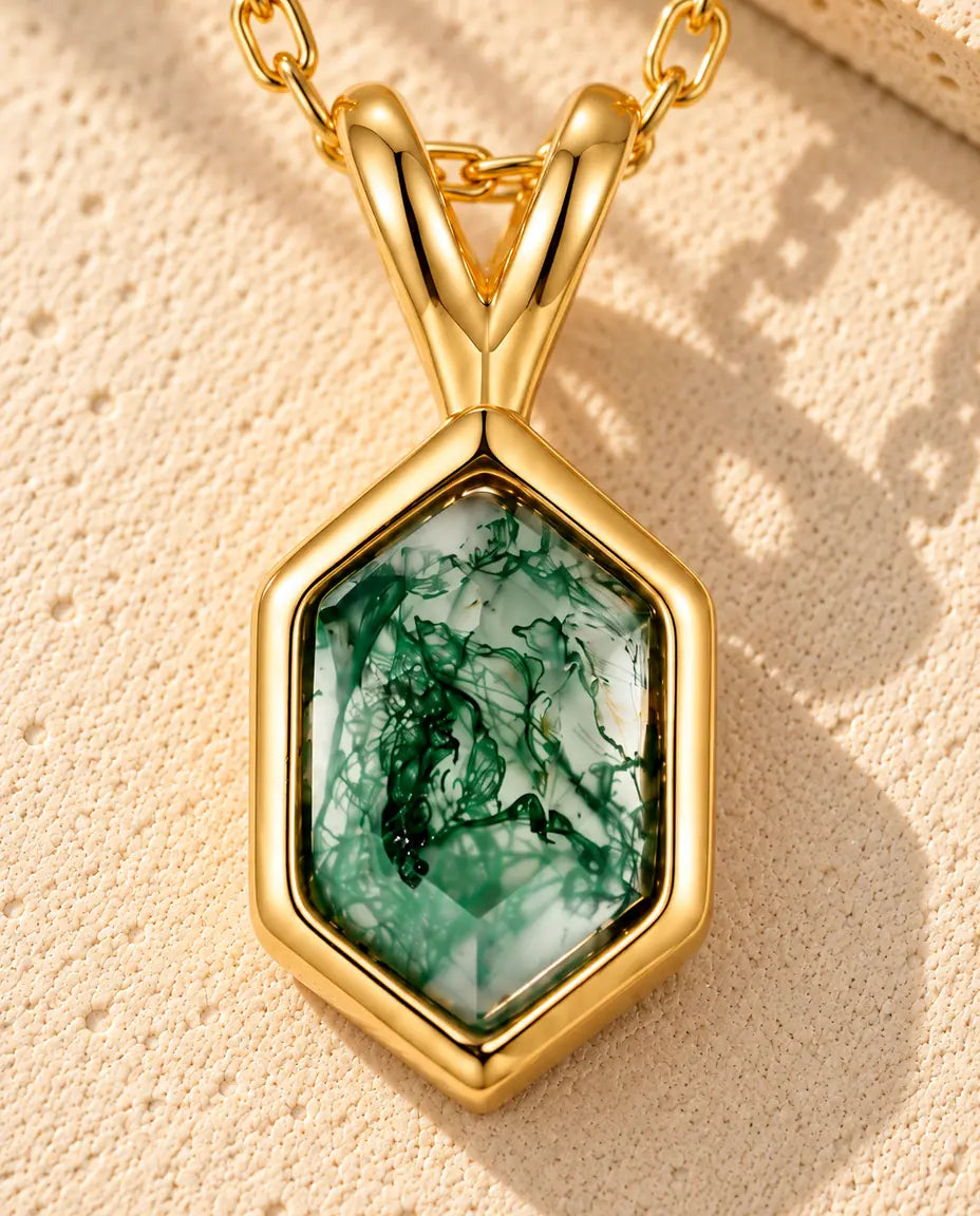 Moss Agate Halsband i Guldpläterat 925 Sterlingsilver - liggande på en ljus strukturerad yta bredvid ett travertinblock