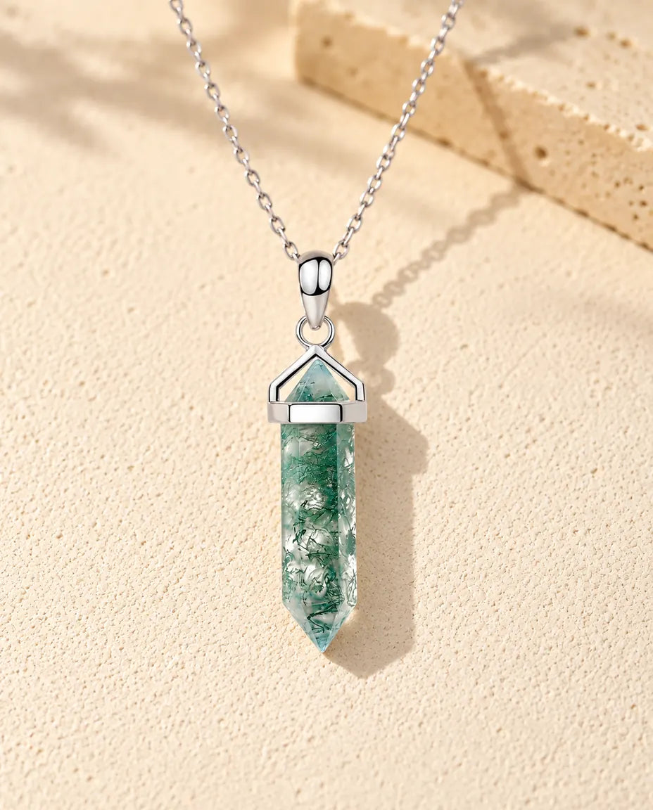 Moss Agate Halsband med Sexkantig Spets i 925 Sterlingsilver - liggande på en ljus strukturerad yta bredvid ett travertinblock