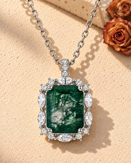 Moss Agate Halsband med Smaragdslipad Sten i 925 Sterlingsilver - liggande på en ljus strukturerad yta bredvid ett travertinblock