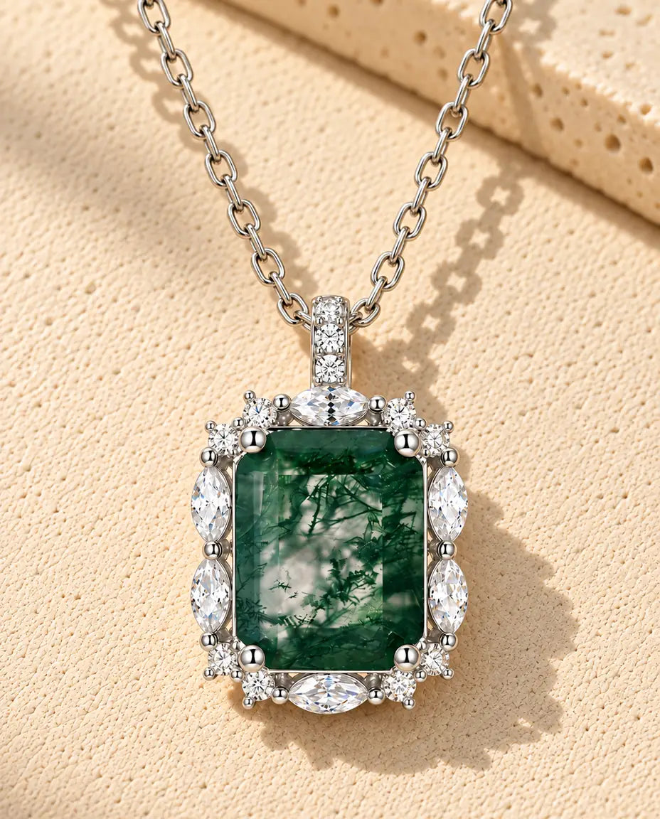 Moss Agate Halsband med Smaragdslipad Sten i 925 Sterlingsilver - liggande på en ljus strukturerad yta bredvid ett travertinblock