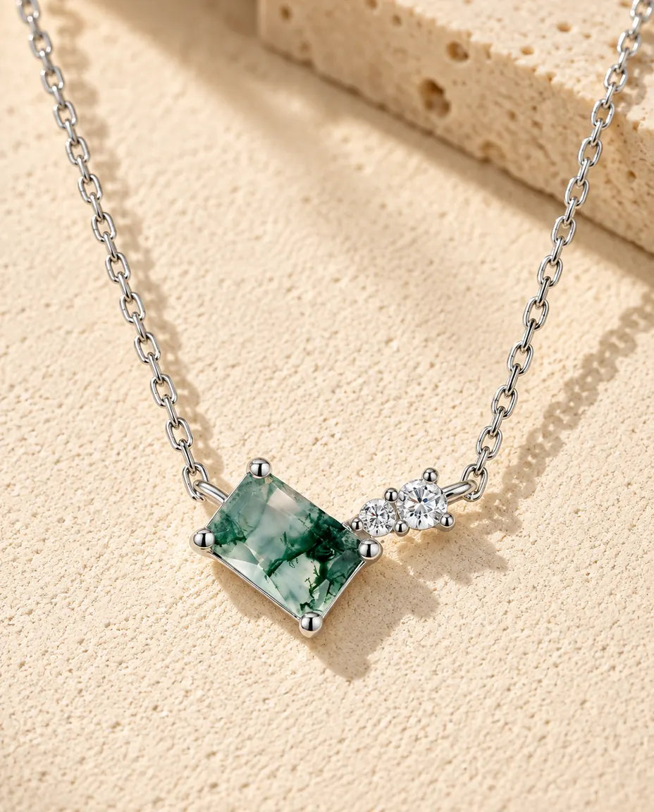 Moss Agate Halsband i 925 Sterlingsilver - liggande på en ljus strukturerad yta bredvid ett travertinblock