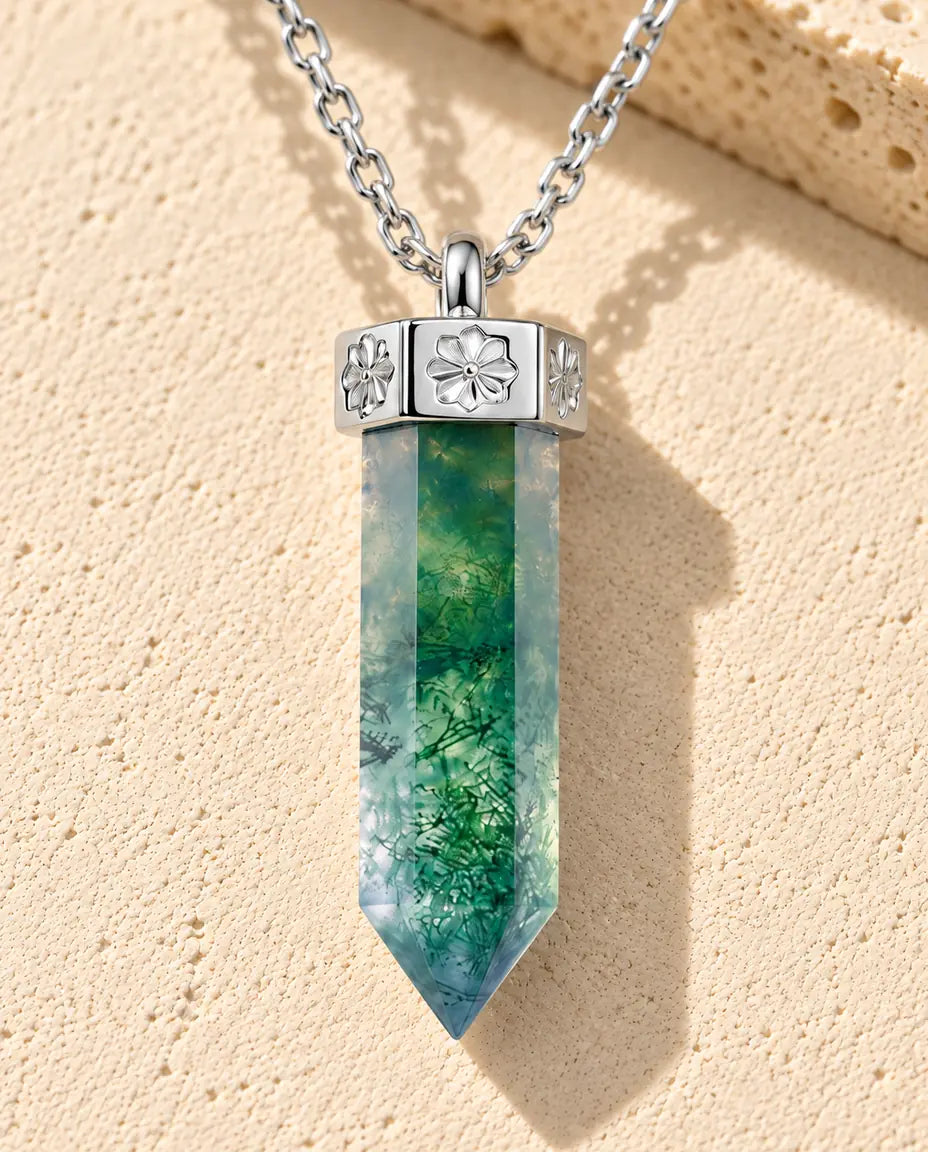 Moss Agate Halsband med Spets i 925 Sterlingsilver - liggande på en ljus strukturerad yta bredvid ett travertinblock