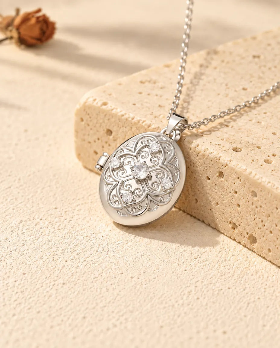 Personligt halsband med silverfärgad oval fotomedaljong, filigranblomma och zirkonia, lutad mot ett travertinblock