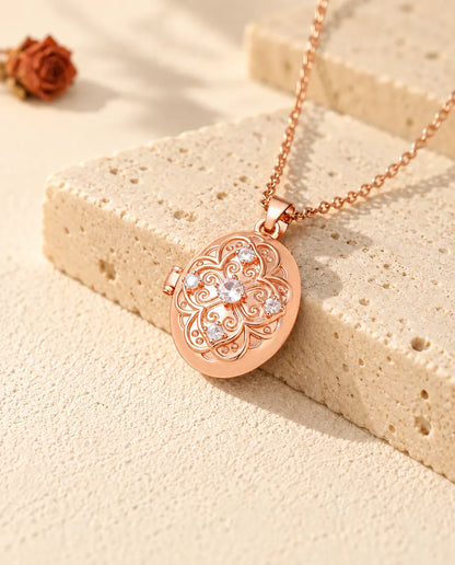 Roséguldfärgad oval fotomedaljong med en blomma av zirkonia på locket, vilande mot travertin