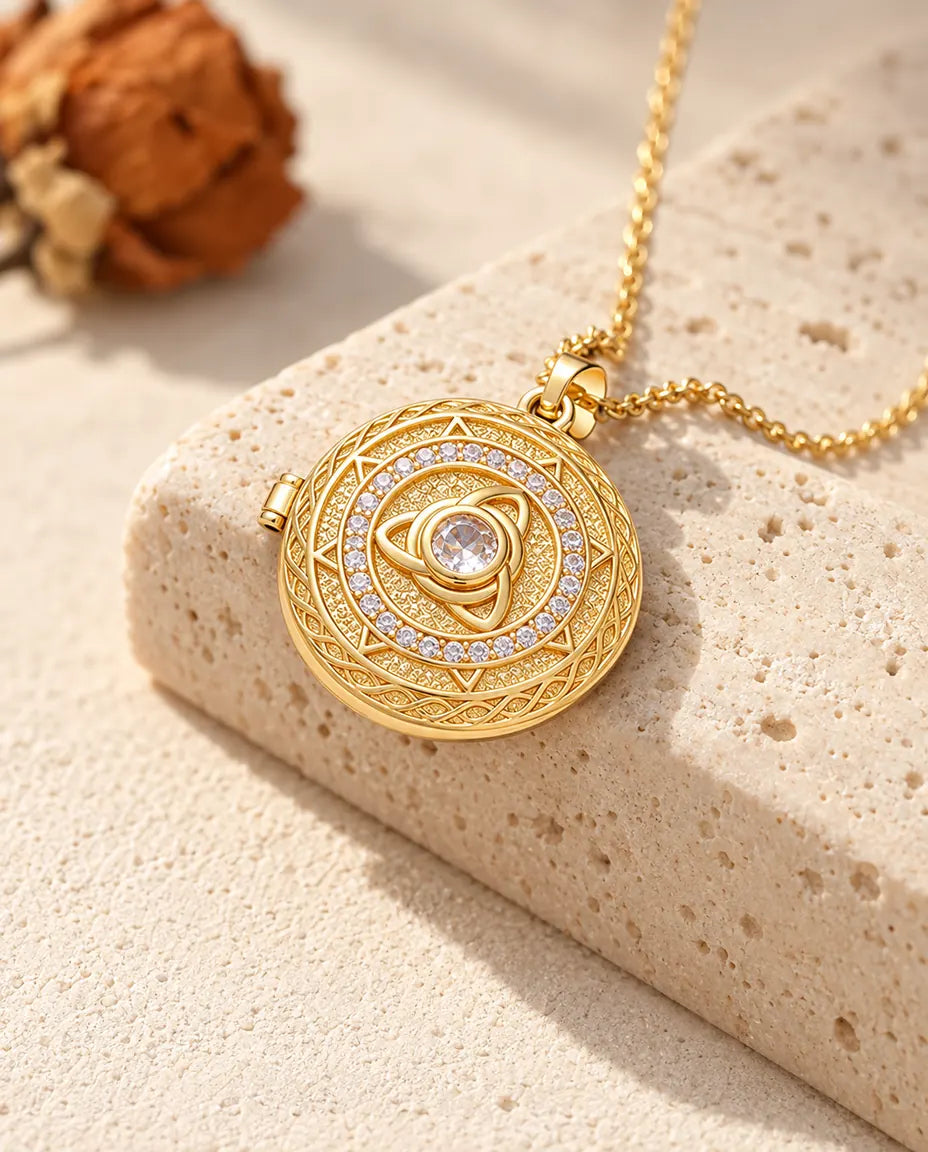 Guldfärgat halsband med rund triquetra-medaljong och stor mittsten, draperat över ett travertinblock