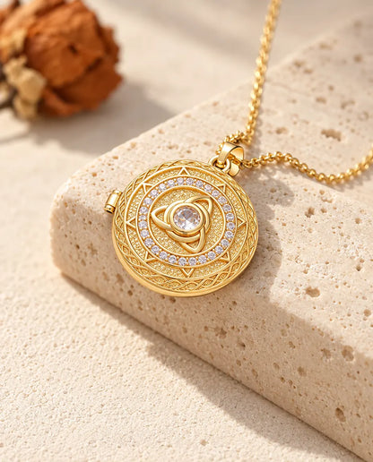 Guldfärgat halsband med rund triquetra-medaljong och stor mittsten, draperat över ett travertinblock