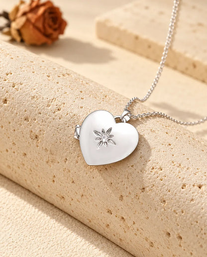 Personlig satinerad hjärtmedaljong i silverfärgat utförande med en liten blomma på locket, lutad mot ett travertinblock