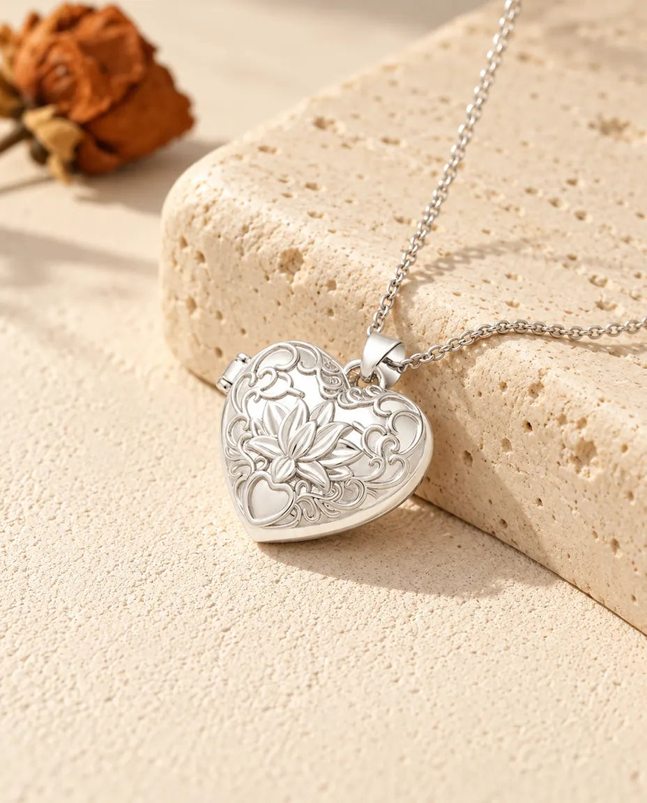 Personlig hjärtmedaljong med lotusblomma och rankor i relief, silverfärgad, lutad mot ett travertinblock
