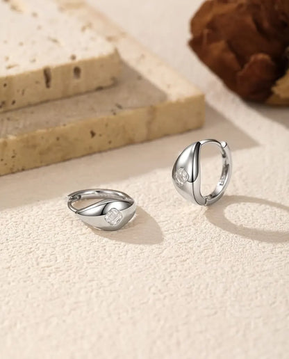 Moissanite Örhängen i 925 Sterlingsilver - paret på en ljus strukturerad yta, ett liggande och ett stående