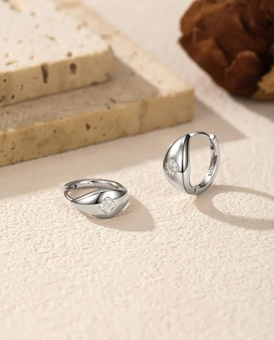 Moissanite Örhängen i 925 Sterlingsilver - paret på en ljus strukturerad yta, ett liggande och ett stående