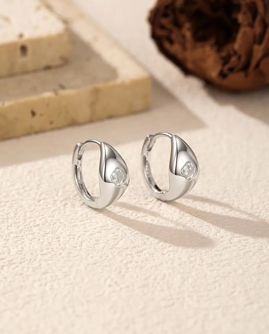 Moissanite Örhängen i 925 Sterlingsilver - paret bredvid varandra på en ljus strukturerad yta