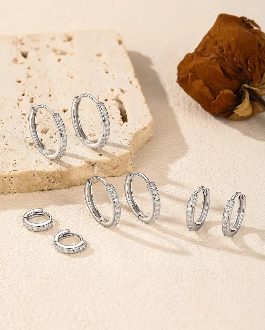 Moissanite Örhängen i 925 Sterlingsilver - alla fem storlekarna på en ljus yta vid en travertinplatta