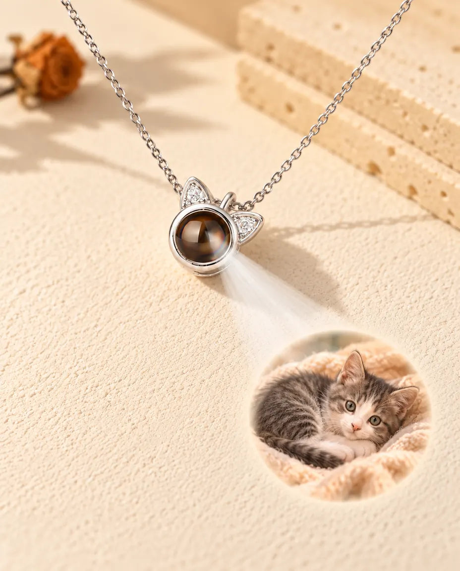 Silverfärgat halsband med kattöron projicerar en bild på en kattunge mot krämvit gips