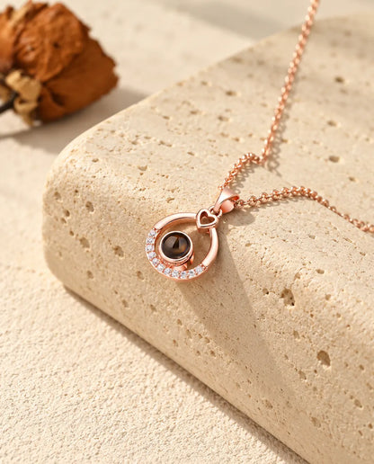 Roséguldfärgat droppformat halsband med bild inuti, hängande över travertin