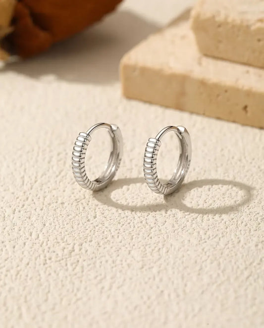 Räfflade Små Creoler i 925 Sterlingsilver - paret bredvid varandra på en ljus strukturerad yta
