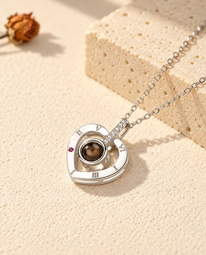 Personligt halsband i 925 sterlingsilver med romerska siffror och bild inuti, på krämvit gips bredvid travertin
