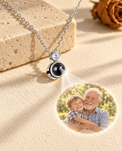 Silverfärgat solitärhalsband projicerar en bild på en äldre man och hans barnbarn mot gips