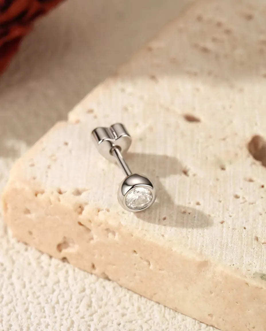 Stiftörhängen med Moissanit i Zargfattning i 925 Sterlingsilver - på en ljus strukturerad yta bredvid en travertinplatta