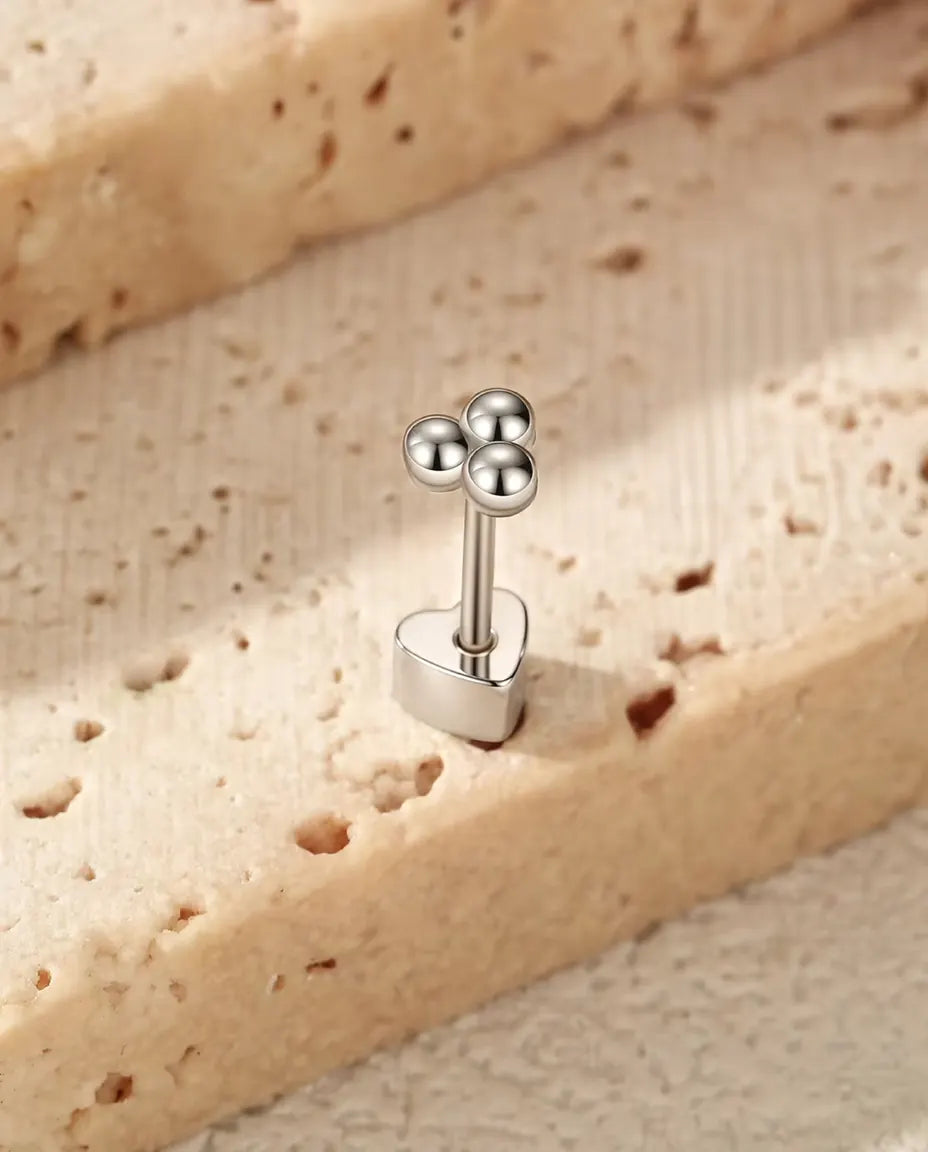Stiftörhängen i Klöverform med Tre Silverkulor i 925 Sterlingsilver - stående på det hjärtformade låset, på en ljus strukturerad yta