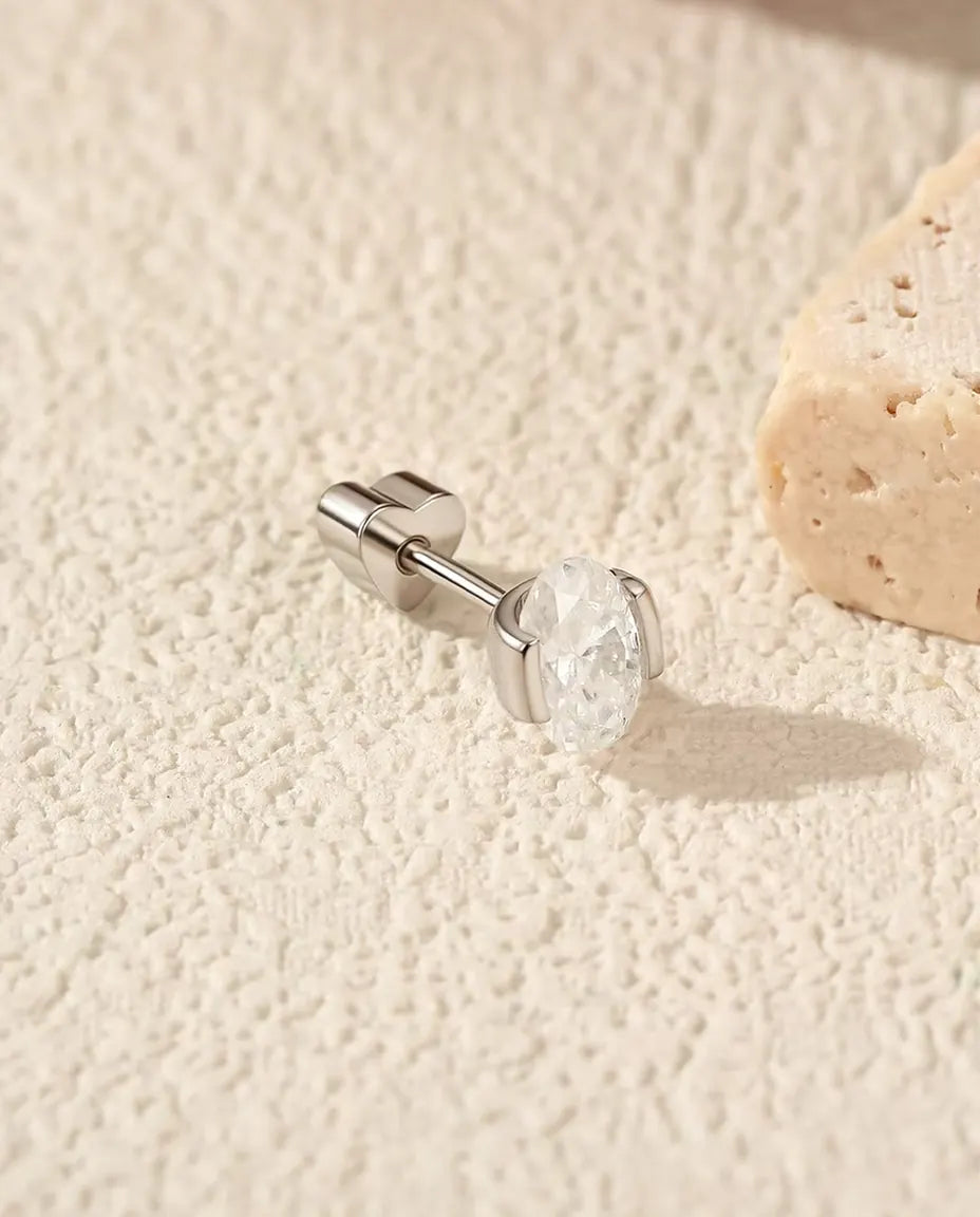 Stiftörhängen med Oval Moissanit i Sidofattning i 925 Sterlingsilver - liggande på sidan på en ljus strukturerad yta, hjärtformat lås på stiftet