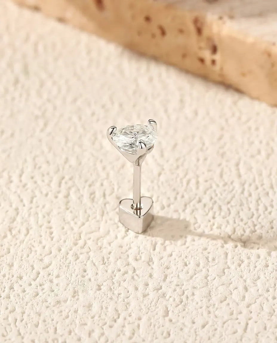 Stiftörhängen med Rund Moissanit i Tre Klor i 925 Sterlingsilver - stående på det hjärtformade låset, på en ljus strukturerad yta