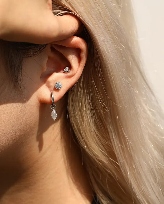 Stiftörhängen med Moissanitesolitär på 5 mm i Fyra Klor i 925 Sterlingsilver - buret av en modell som stryker håret bakom örat