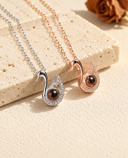 Svanhalsband med bild inuti i silverfärgat och roséguldfärgat liggande på krämvit gips